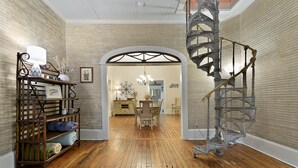 A spacious room with a wooden floor, a spiral staircase, and a dining area with a chandelier. - Carroll House Cottages (Bay St Louis)