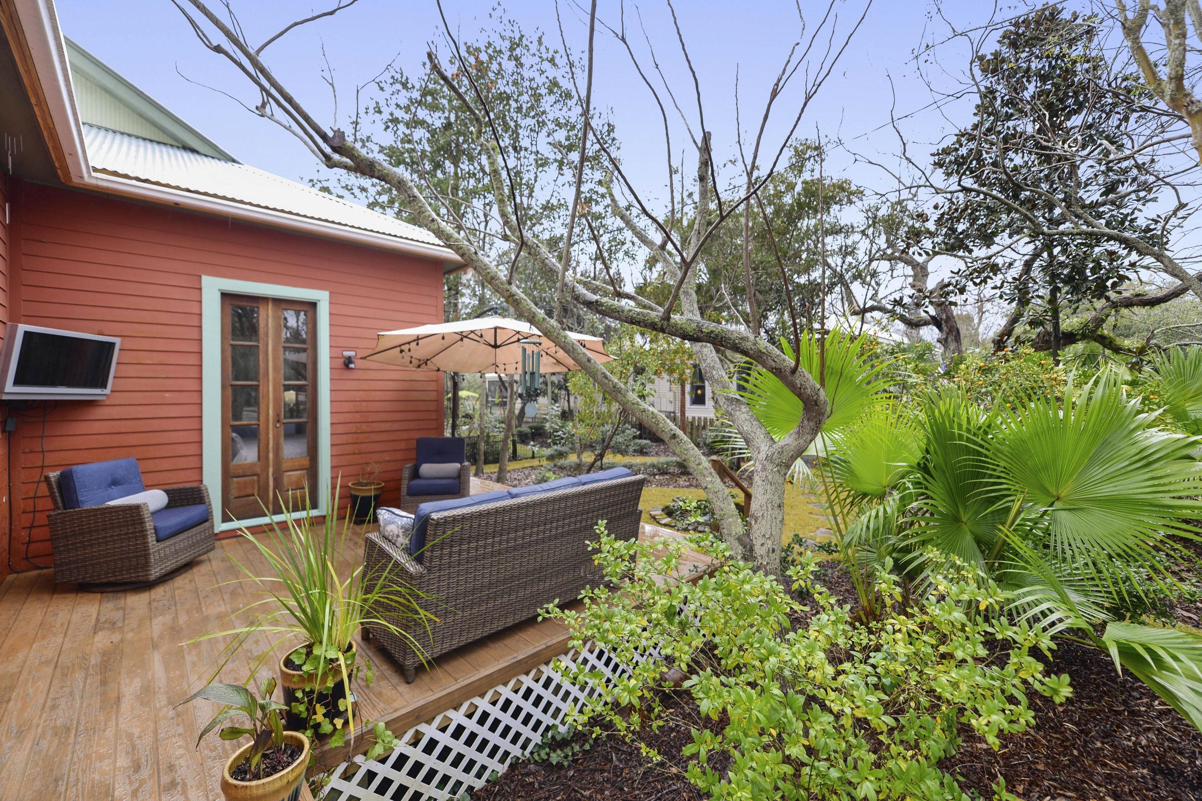 A red house with a deck, outdoor furniture, and a variety of plants.
