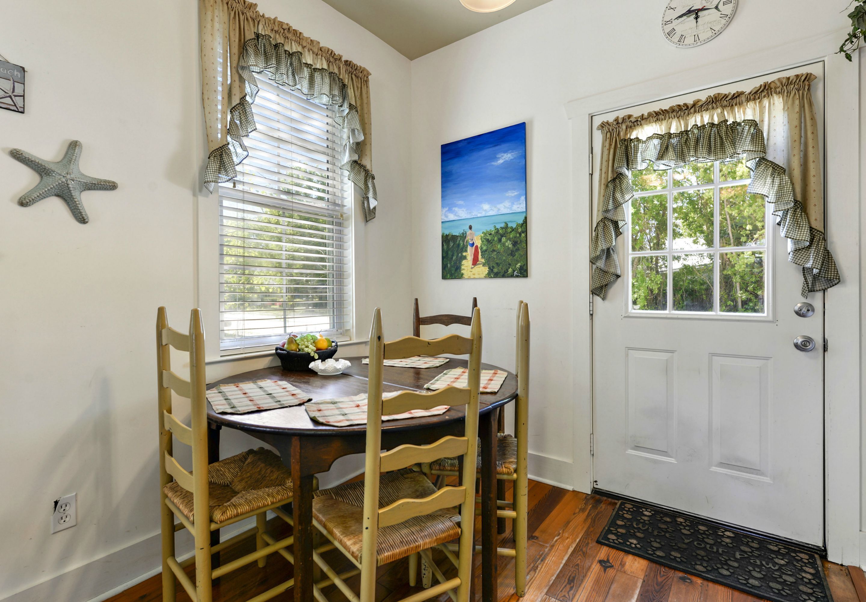 A dining area with a round table, four chairs, a starfish decoration, a painting, and a door with curtains.