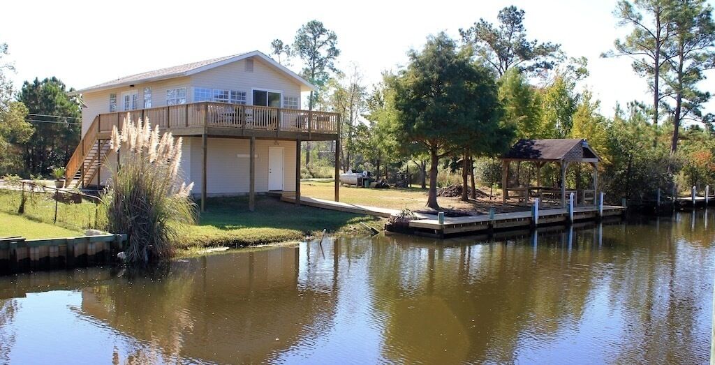 A house with a deck and a dock extending into a calm lake, surrounded by trees.