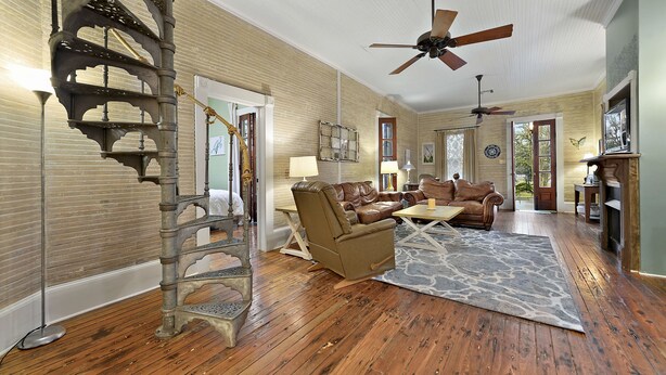 A spacious living room with hardwood floors, a brown leather sofa, a recliner, and a spiral staircase. - Carroll House Cottages (Bay St Louis)