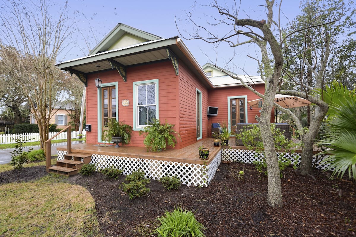 A red house with a porch, white picket fence, and a small garden.