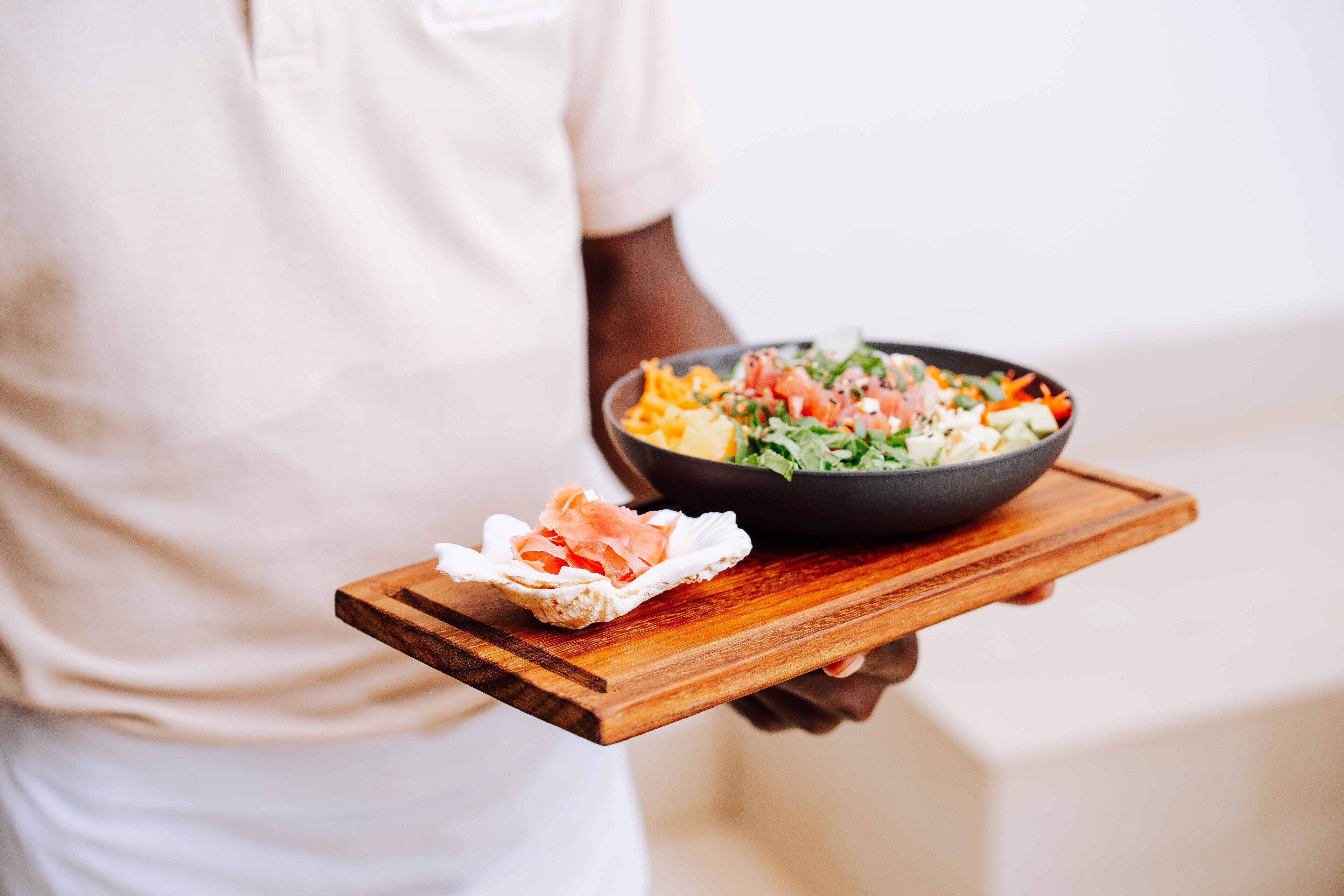 Una persona sostiene una bandeja de madera con una ensalada en un tazón y un trozo de salmón.
