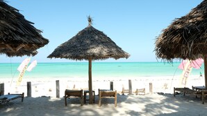 A beach with thatched umbrellas, wooden chairs, and a sandy beach. - Dhow Inn Boutique Hotel (Paje)