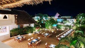 A beachside restaurant with thatched-roof structures, outdoor seating, and lush greenery. - Dhow Inn Boutique Hotel (Paje)
