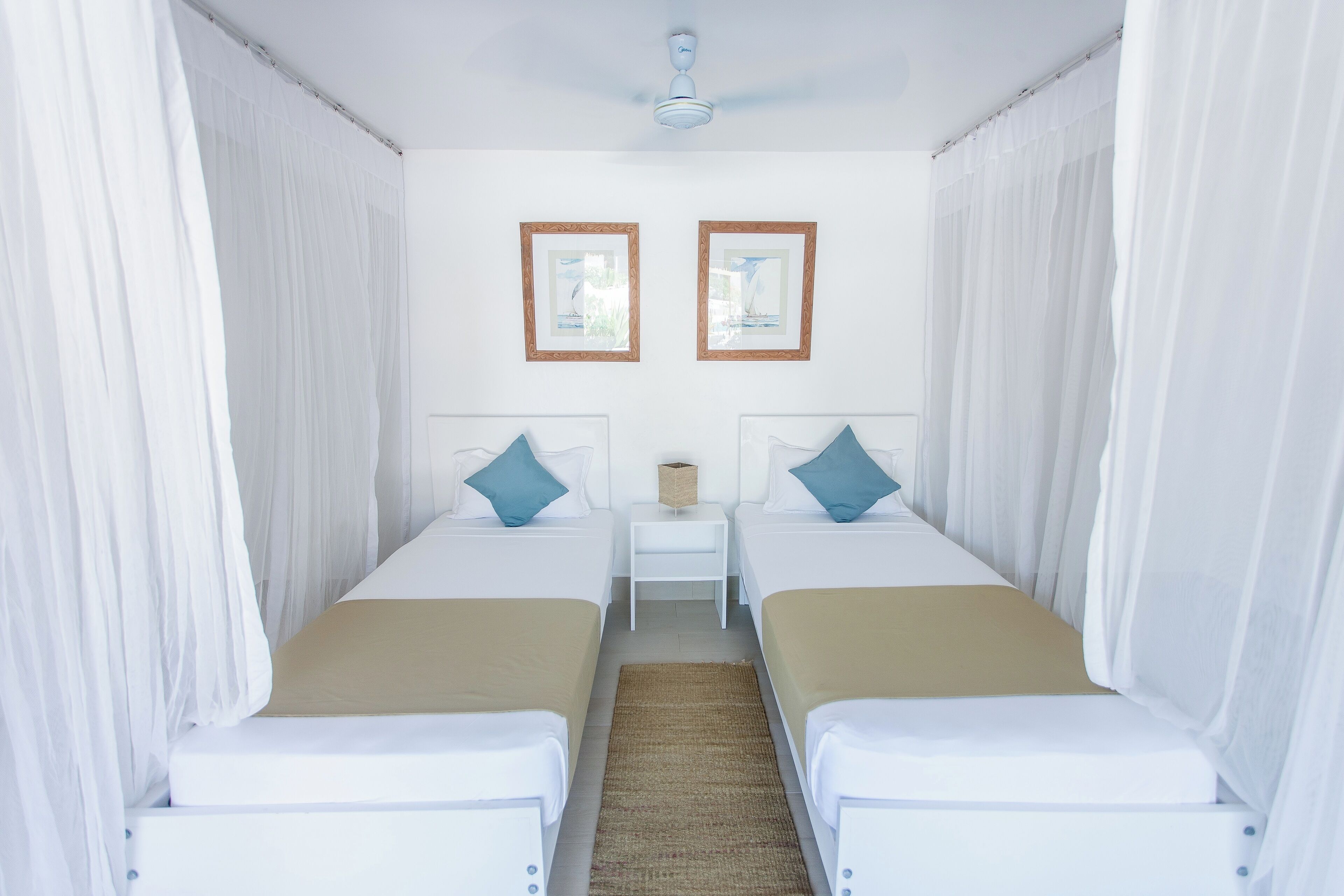 Una habitación con dos camas, una mesita y dos cuadros en la pared.