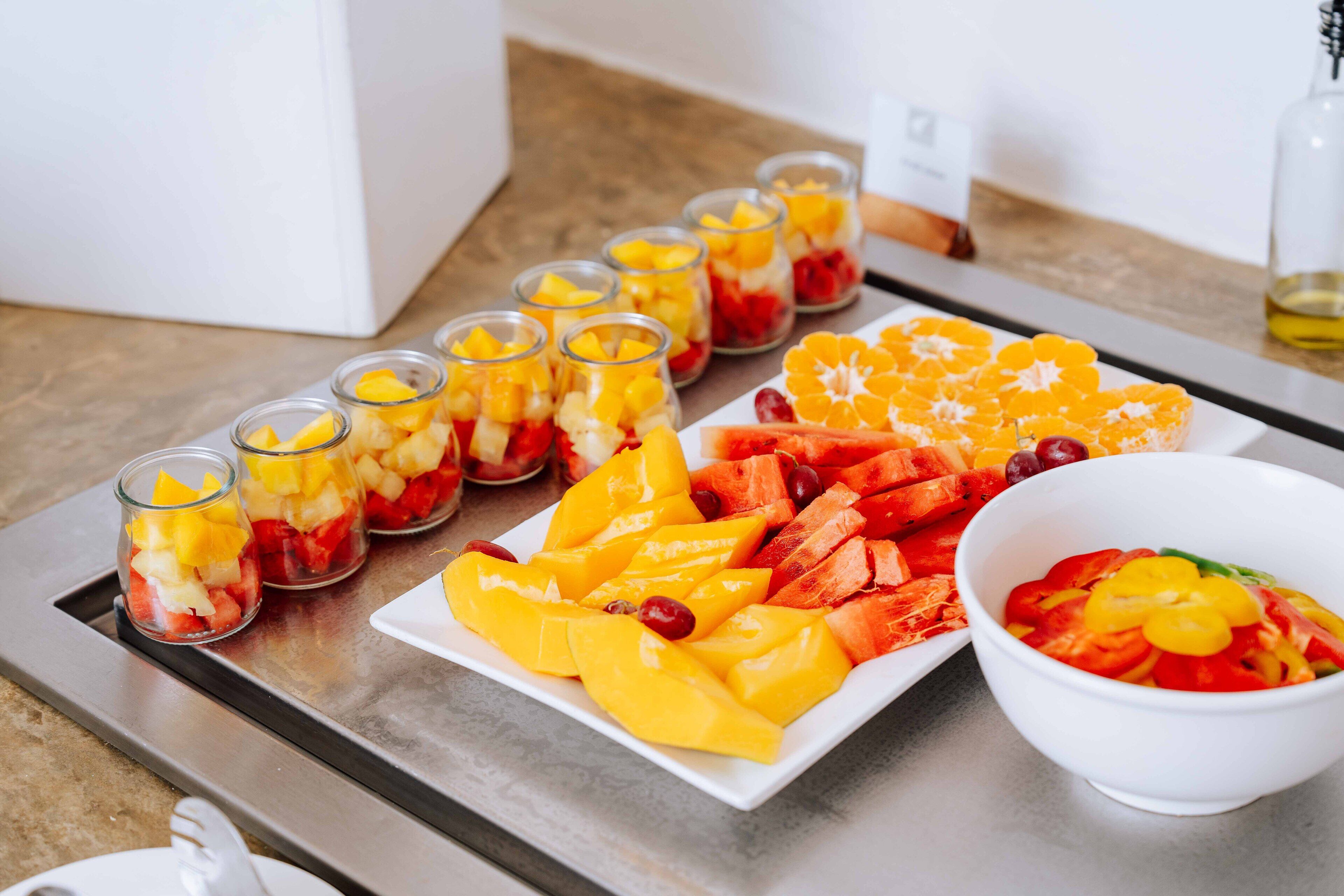 Een dienblad met verschillende fruitcreaties, waaronder partjes sinaasappel en mango's, en een kom fruitsalade.
