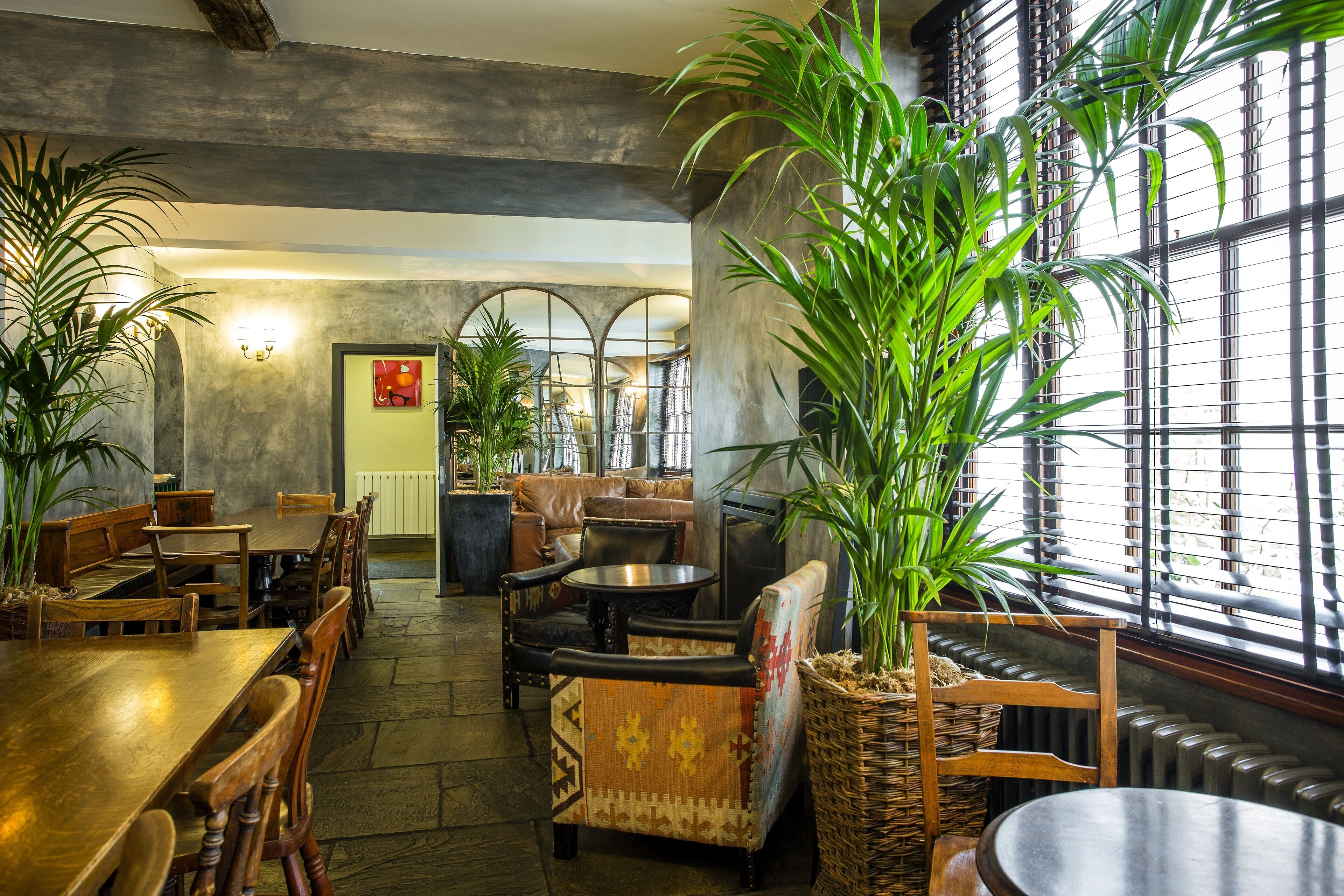 A spacious indoor area with a long wooden table, several chairs, a sofa, and a large potted plant.