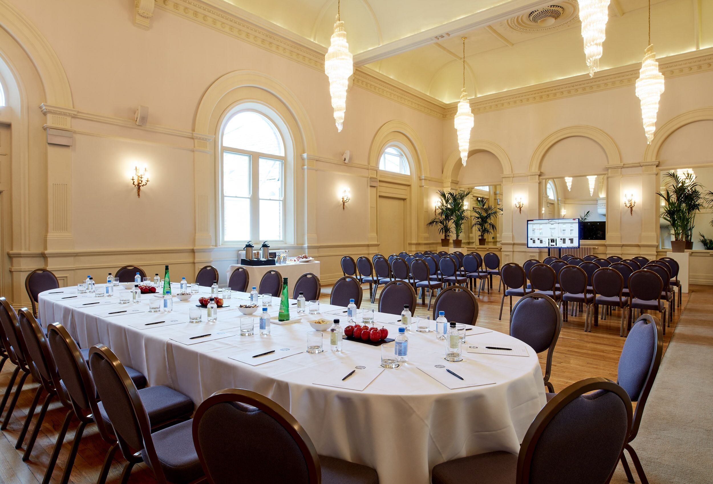 A large conference room with a long table set for a meeting, surrounded by chairs, and equipped with water bottles and snacks.