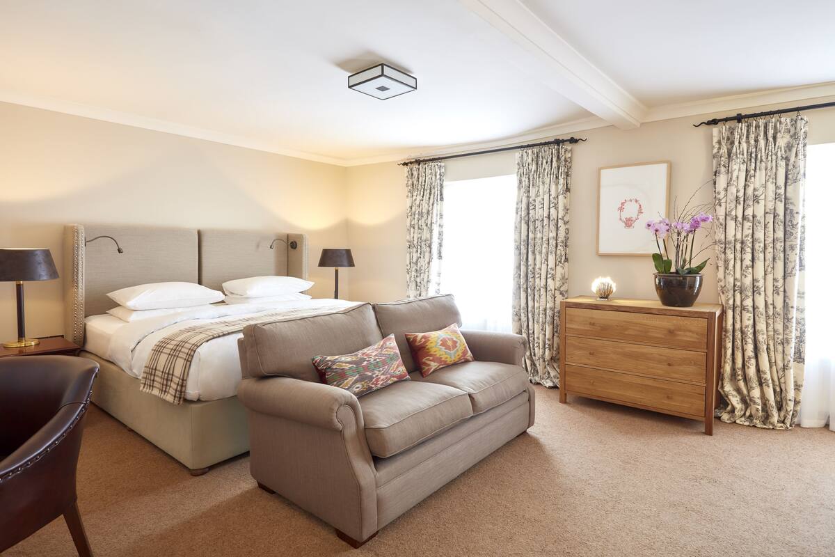 A bedroom with a bed, a sofa, a wooden dresser, and a desk with a lamp.