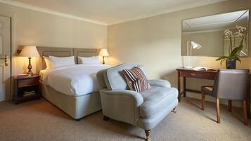 A hotel room with a bed, a desk, a chair, a nightstand, and a lamp.