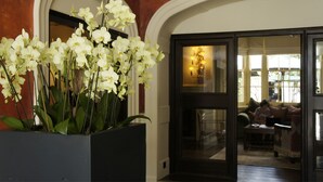 A reception area with a large orchid plant, a dark wooden door, and a view into a room with a sofa and a lamp. - The Angel Hotel Abergavenny (Abergavenny)