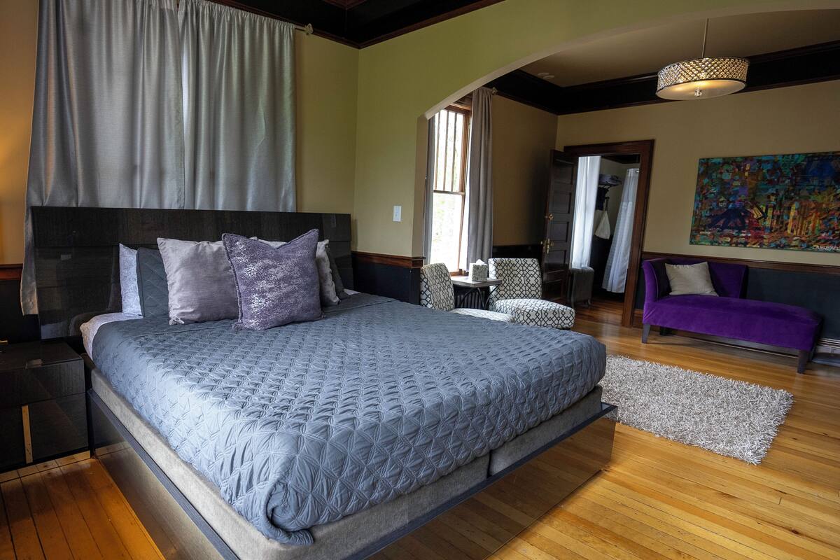 A bedroom with a large bed, a sofa, a chair, and a painting on the wall.