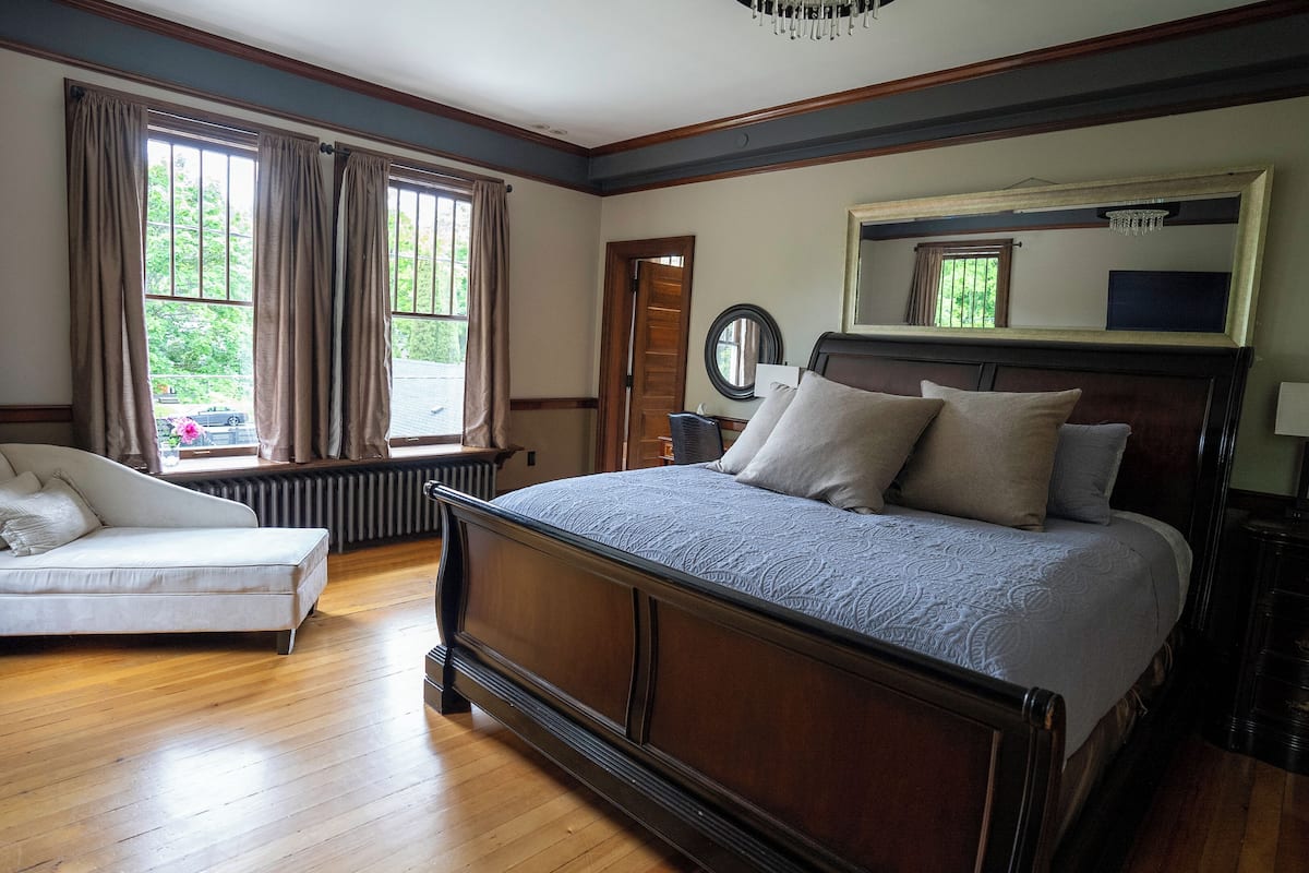 A bedroom with a large bed, a chair, a dresser, a mirror, and a window with curtains.