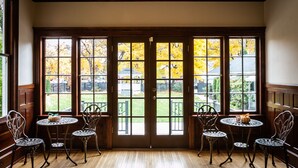 A room with a wooden floor, a large window with a view of autumn trees, and four metal chairs around a small table. - Blackwell Hotel (Coeur d'Alene)
