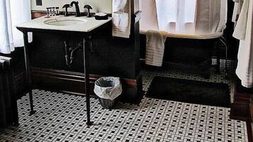Un baño con un espejo redondo, dos apliques de pared, un lavabo, un perchero para toallas y una cortina de ducha.