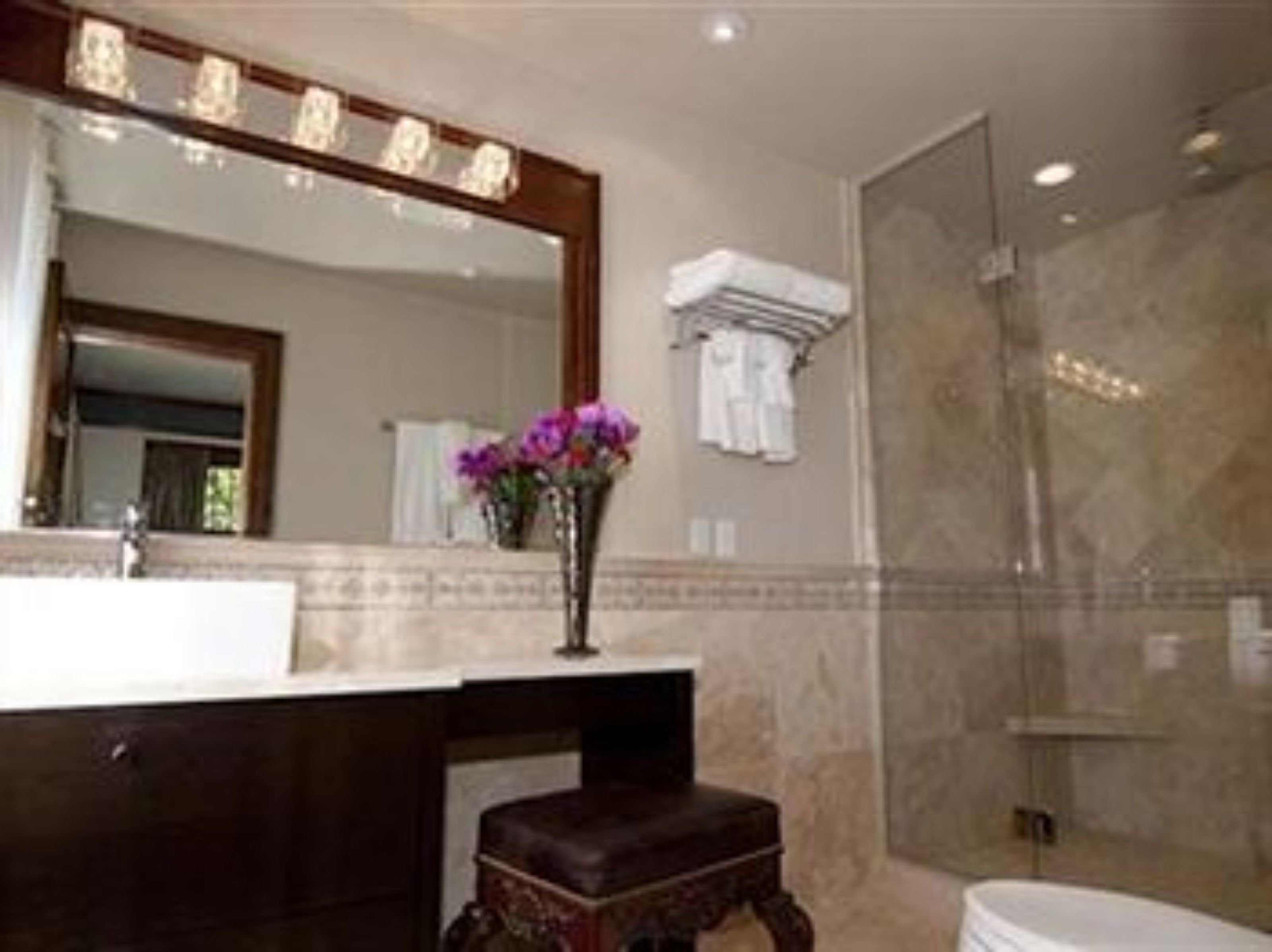 Une salle de bain avec un grand miroir, un lavabo, un vase de fleurs et un espace douche.