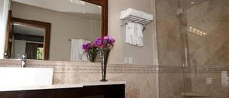 Une salle de bain avec un grand miroir, un lavabo, un vase de fleurs et un espace douche.