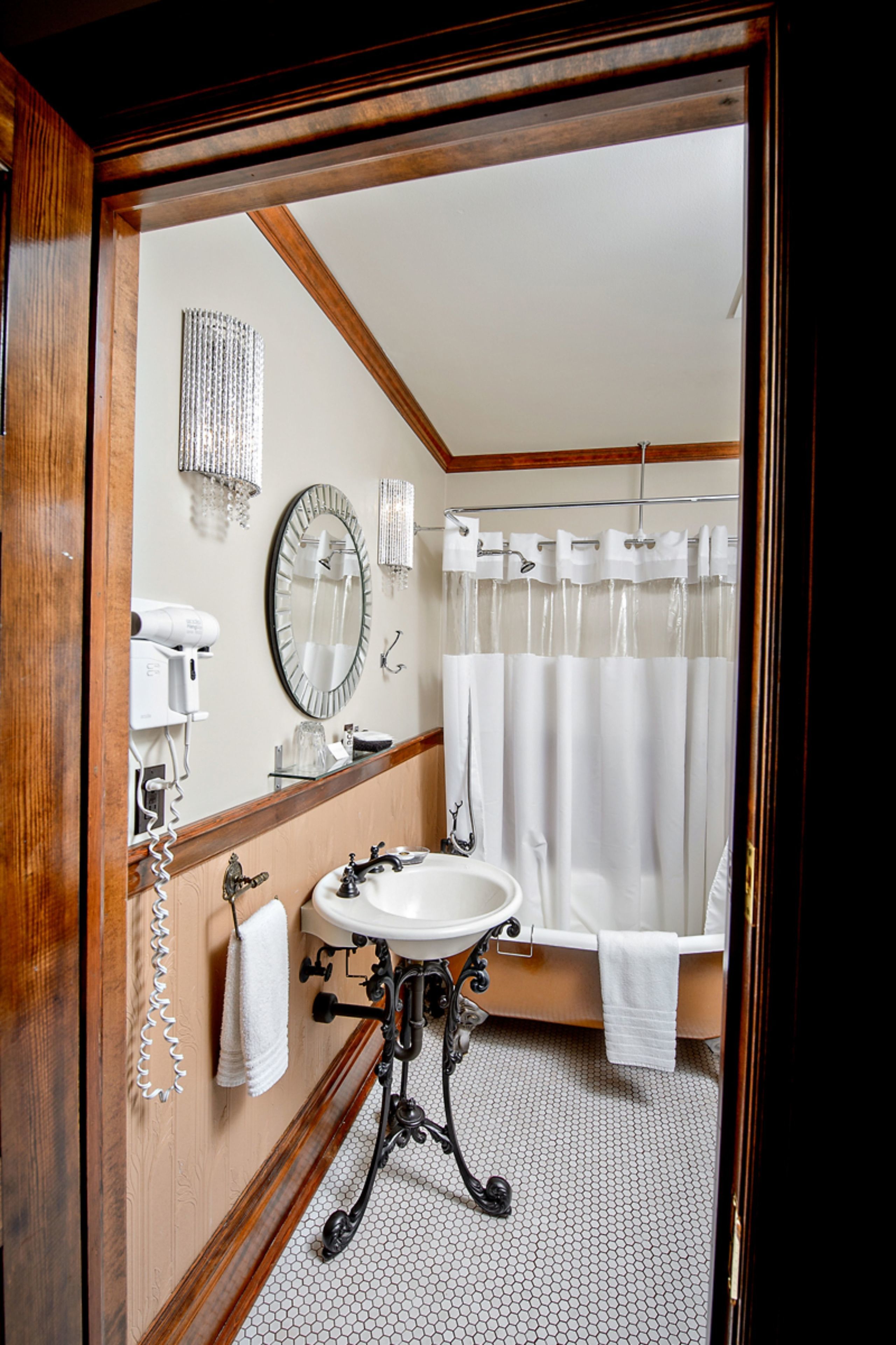 Un baño con tocador de madera, un lavabo, un espejo, cortina de ducha y un perchero para toallas.