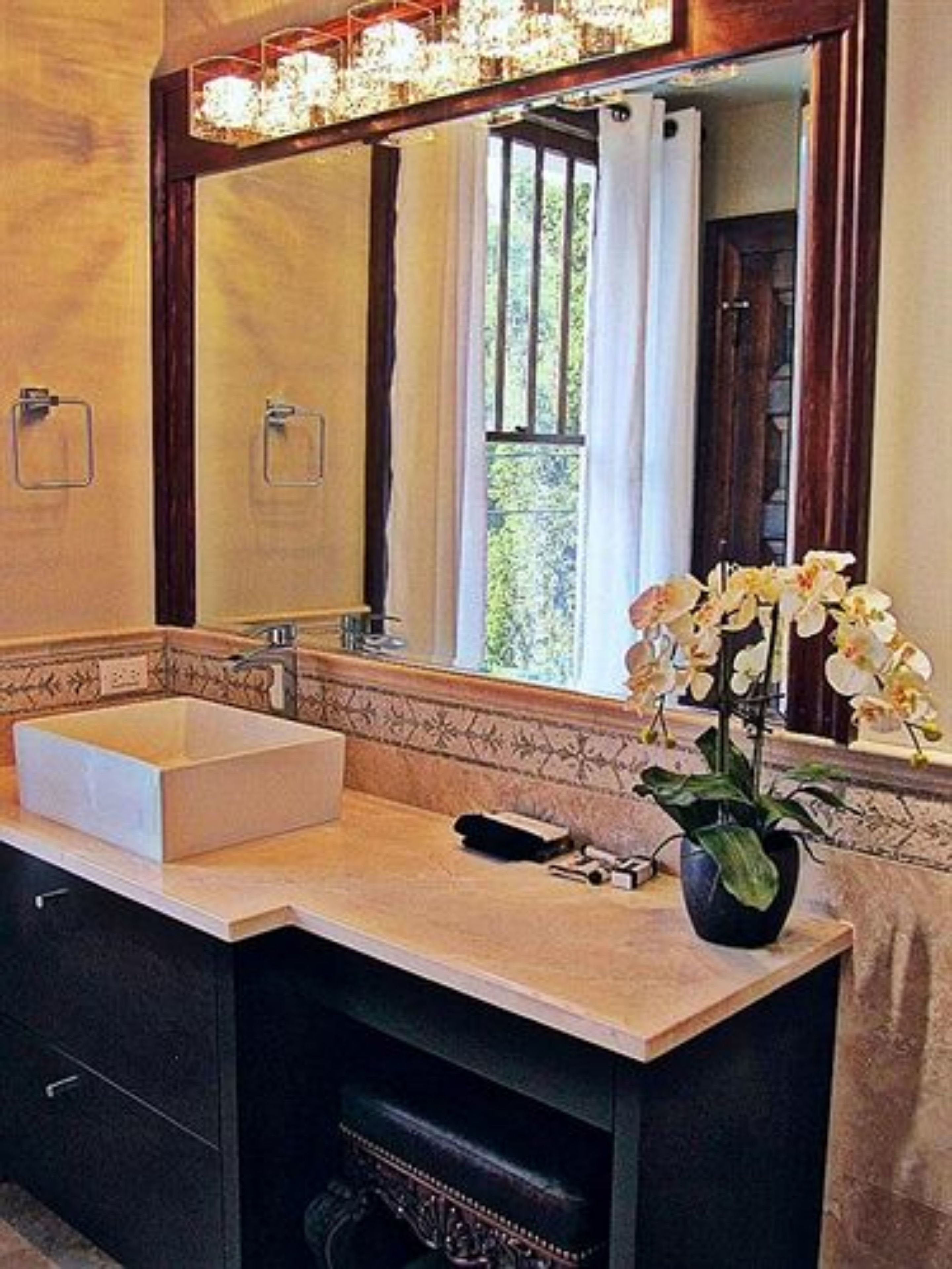 A bathroom with a large mirror, a white sink, and a potted orchid.
