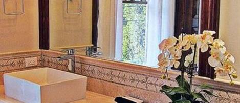 A bathroom with a large mirror, a white sink, and a potted orchid.