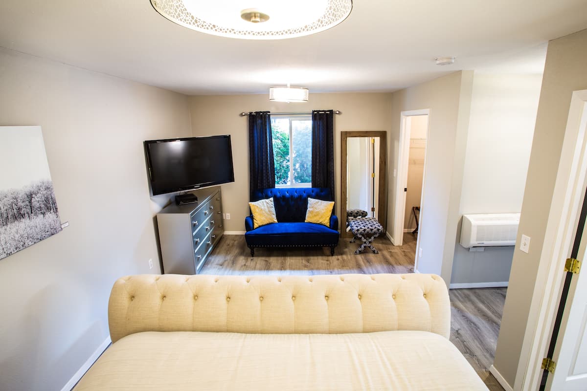 A bedroom with a bed, a TV, a sofa, and a window with curtains.