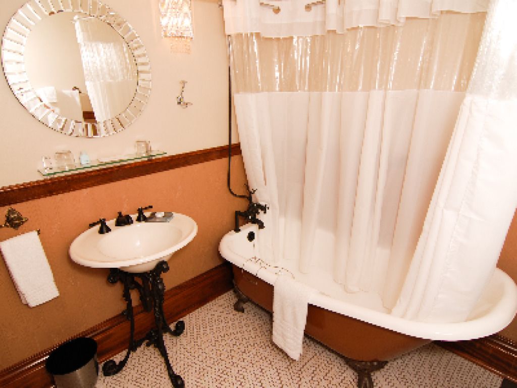 A bathroom with a white sink, a round mirror, and a clawfoot bathtub.