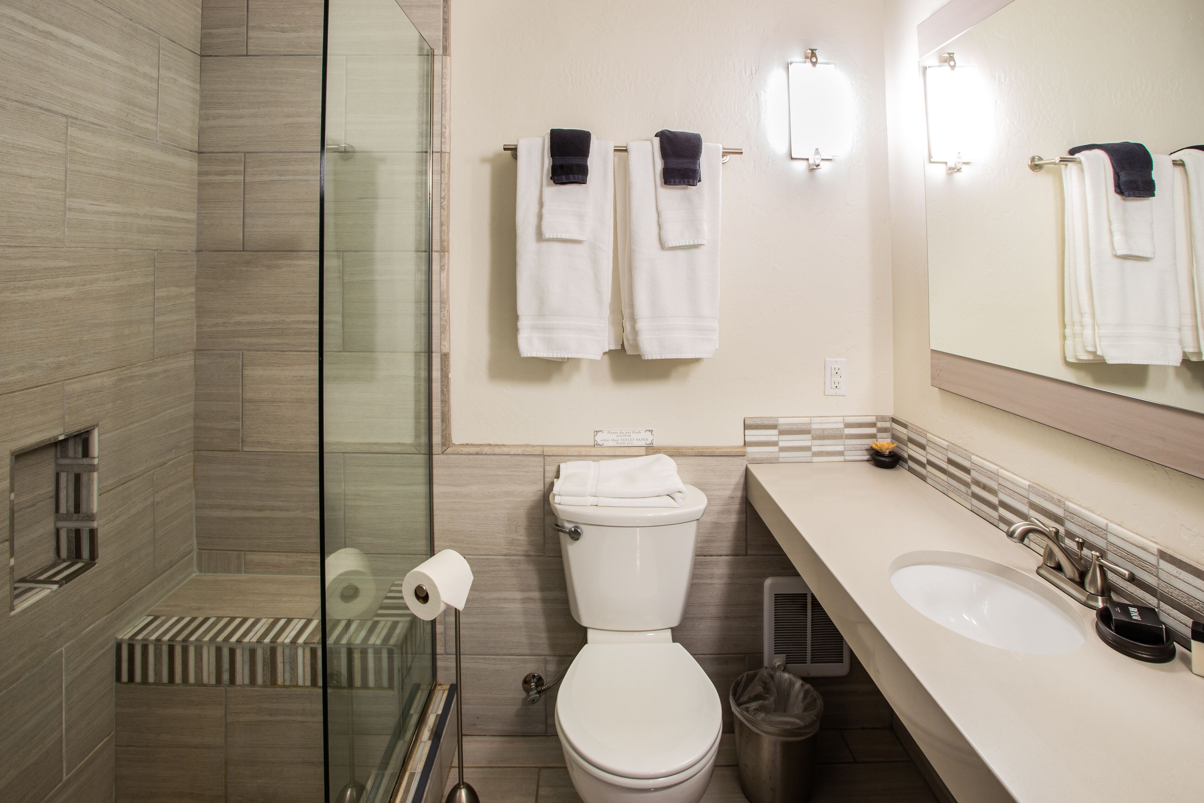 A modern bathroom with a glass shower enclosure, a toilet, a sink, and a mirror.