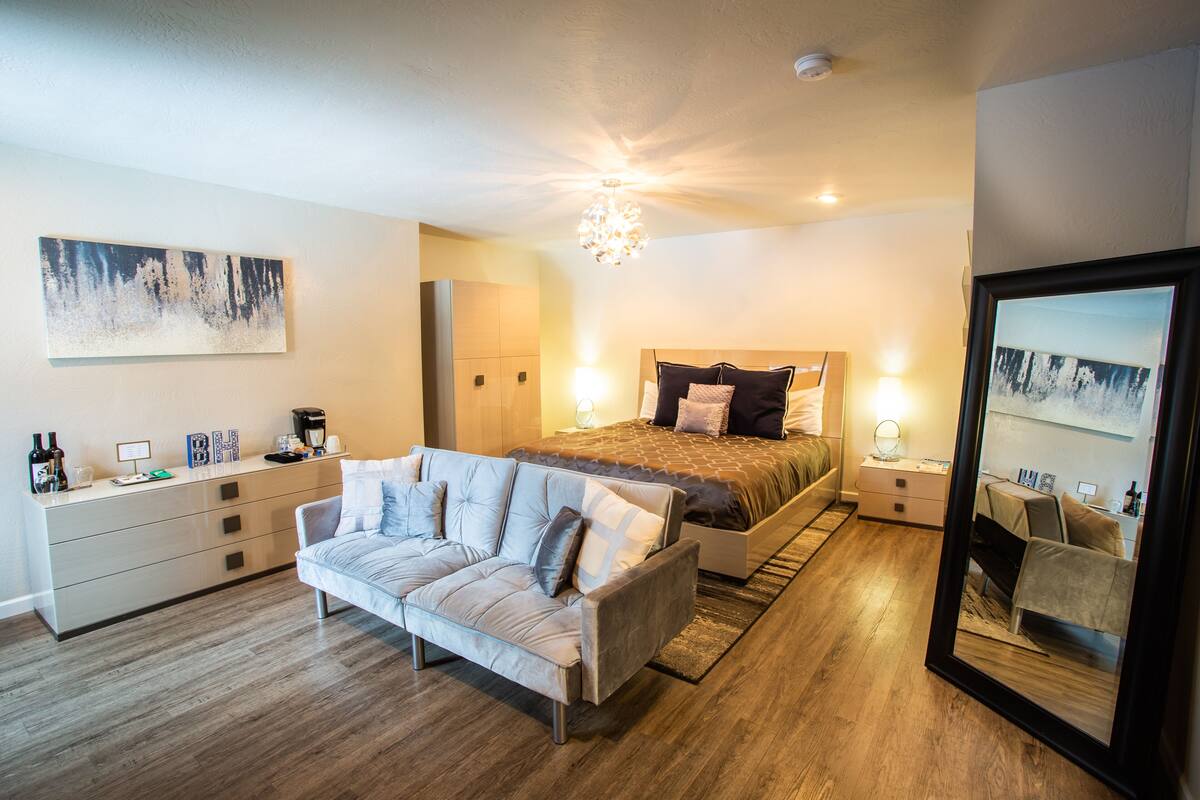A modern bedroom with a large bed, a sofa, a dresser, and a mirror.