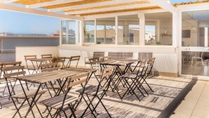 An outdoor patio with wooden tables and chairs, a glass enclosure, and a view of the cityscape. - Nonna Nina (Avola)