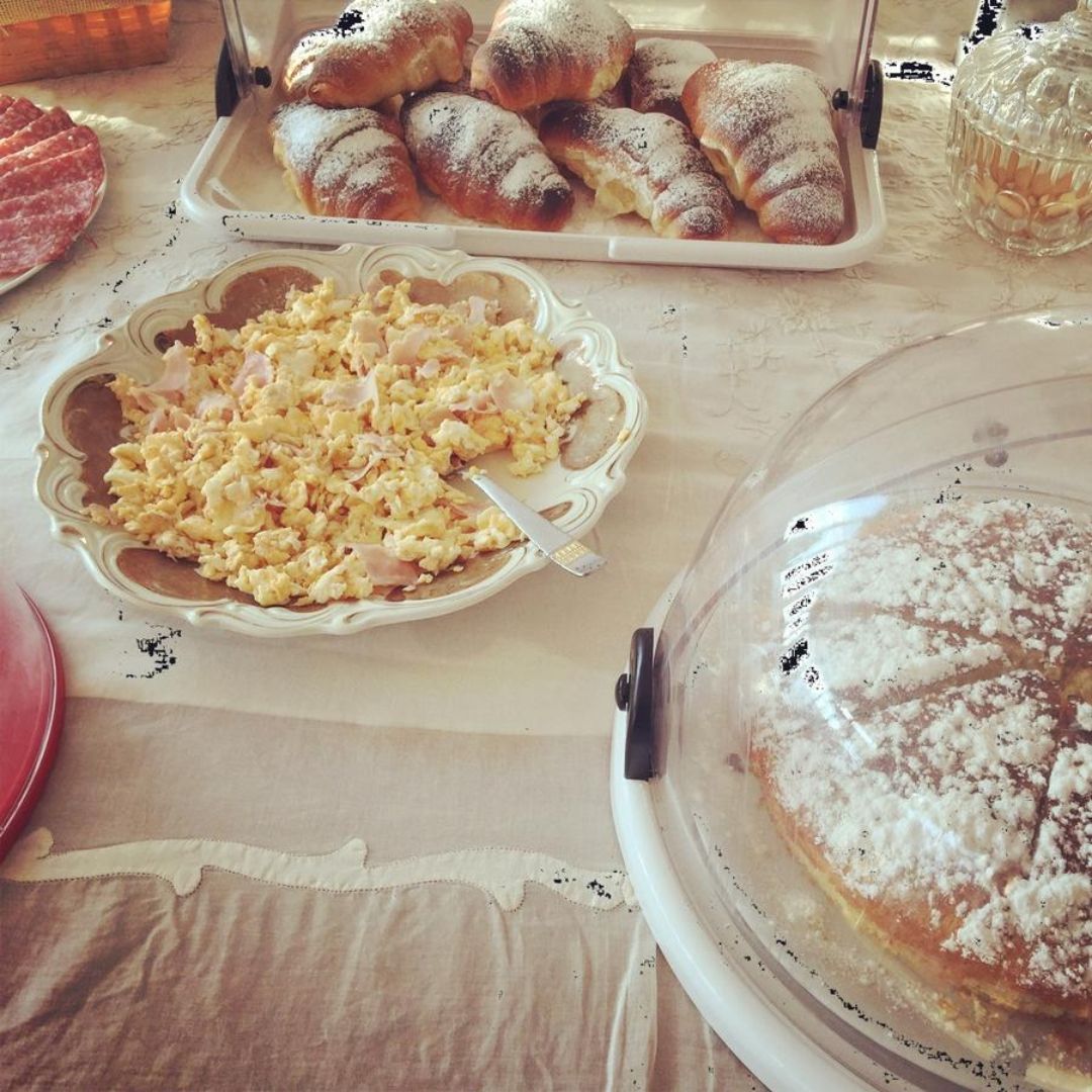 Ein Frühstücksbuffet mit Gebäck, Rührei und einer abgedeckten Schale, vermutlich mit Dessert.