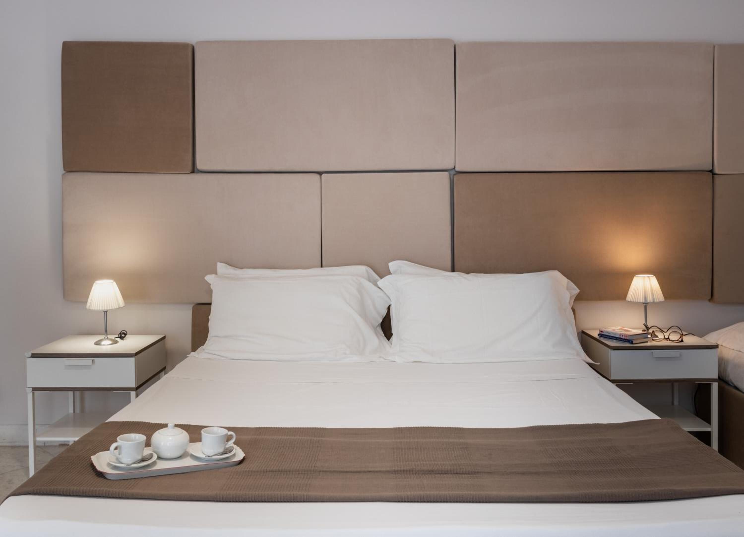A modern hotel room with a large bed, two bedside tables, and a tray with cups and a teapot.