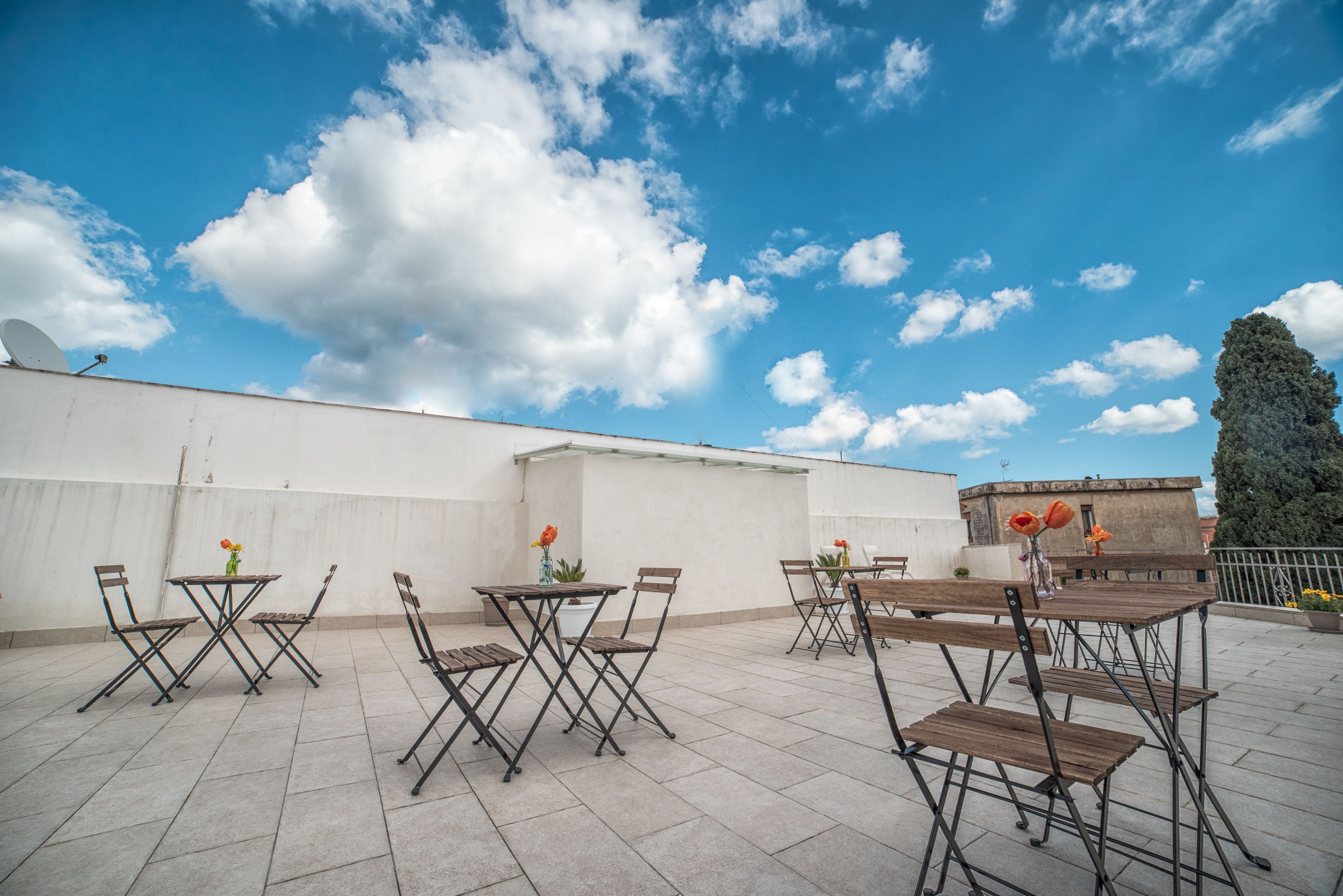 An outdoor patio with multiple tables and chairs, some with flowers.