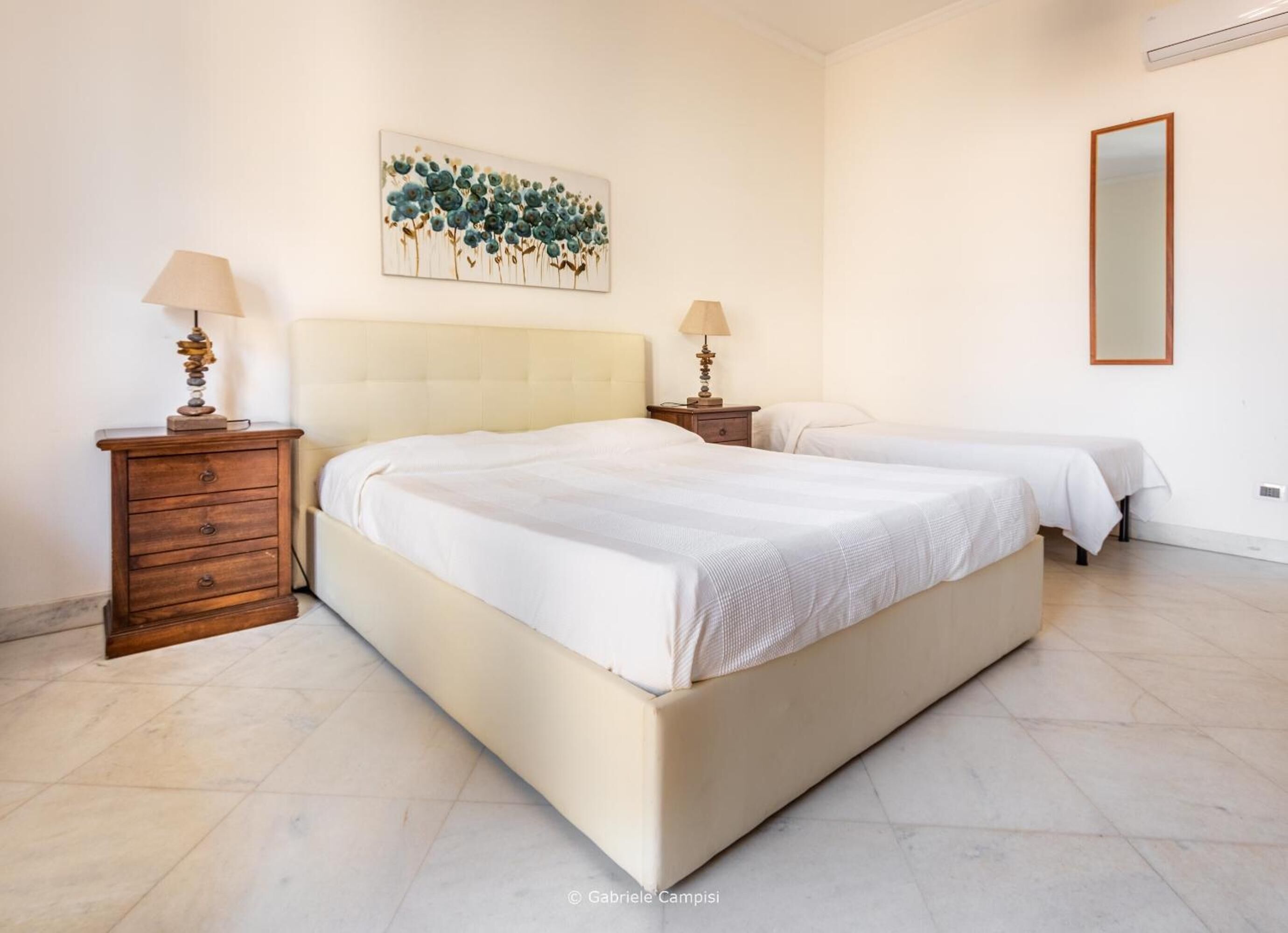 Un dormitorio con una cama grande, dos mesitas de noche con lámparas, un espejo y una obra de arte colgada en la pared.