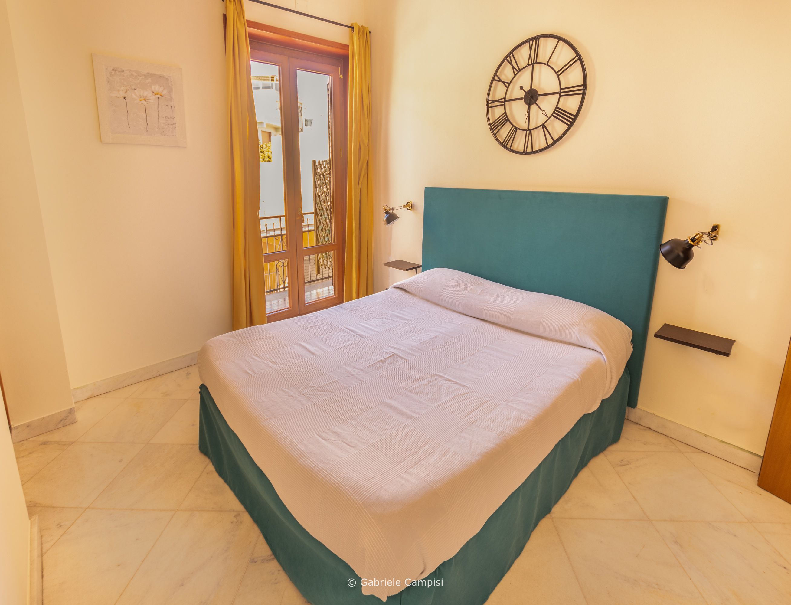 A bedroom with a bed, a clock, and a view through a door.