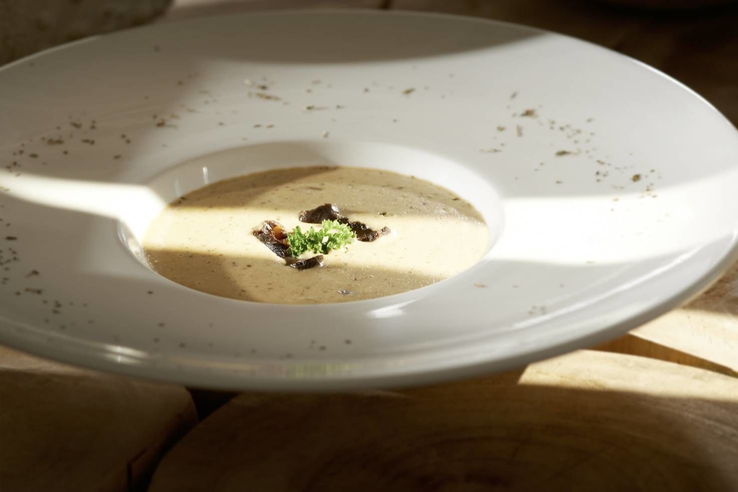 Ein weißer Teller mit cremiger Suppe und einer Garnitur auf einer Holztischplatte.