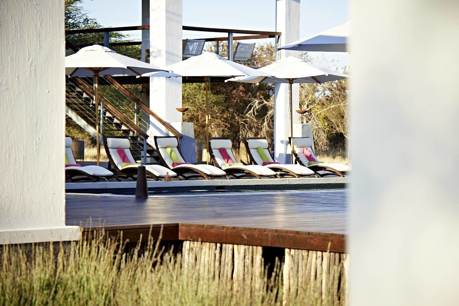 Un espace aménagé au bord de la piscine, avec des chaises longues et des parasols, une terrasse en bois et un escalier menant à un niveau supérieur.