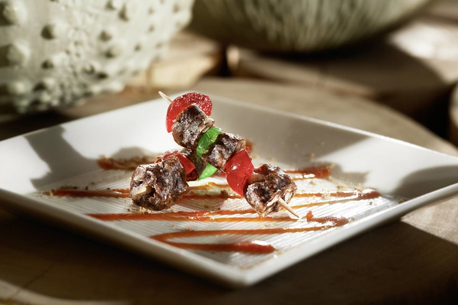 A plate with skewered meat and vegetables, possibly a dish of grilled skewers, on a white plate with sauce drizzled on the side.