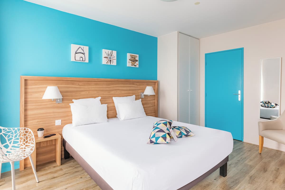 A modern hotel room with a large bed, two bedside tables, a chair, and a bright blue accent wall.
