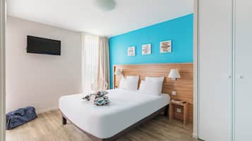A modern hotel room with a large bed, a flat-screen TV mounted on the wall, and a wooden headboard.