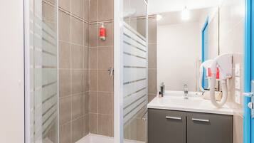 A modern bathroom with a glass-enclosed shower, a sink with a mirror, and a towel dispenser.