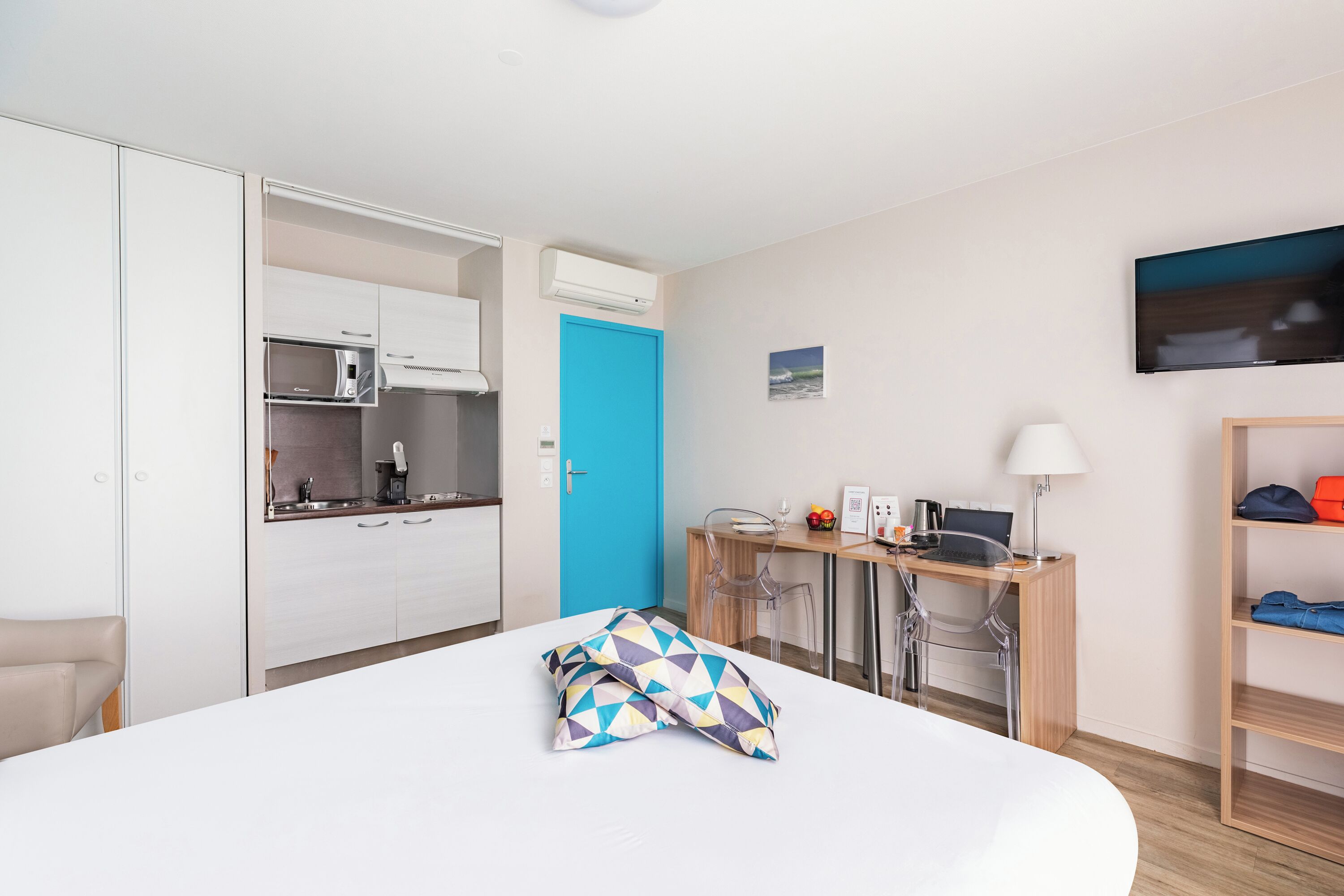 Habitación de hotel con cama, escritorio con computadora, silla, televisor y kitchenette.