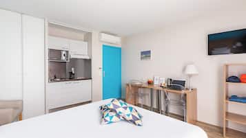 Habitación de hotel con cama, escritorio con computadora, silla, televisor y kitchenette.