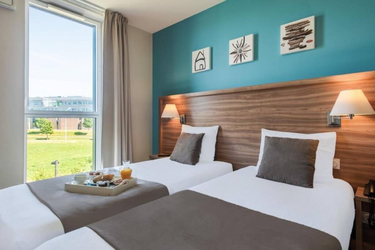 A hotel room with two beds, a large window with a view, and wall art.