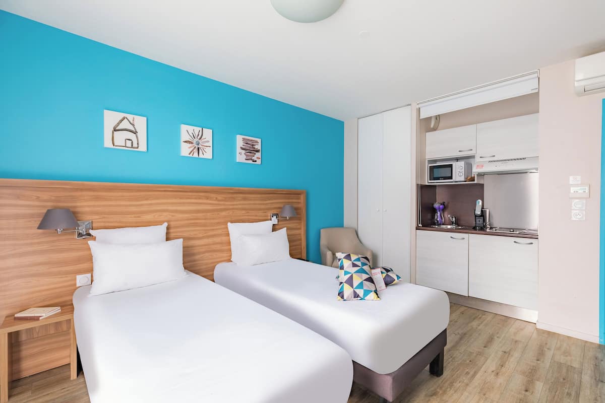 A hotel room with two beds, a kitchenette, and a blue accent wall.