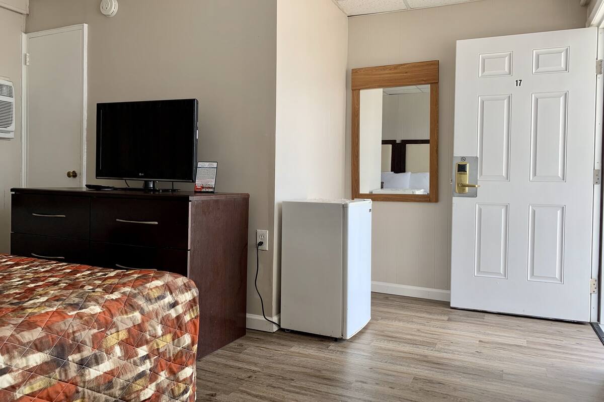 A hotel room with a bed, a TV on a dresser, a refrigerator, a mirror, and a door with the number 17.