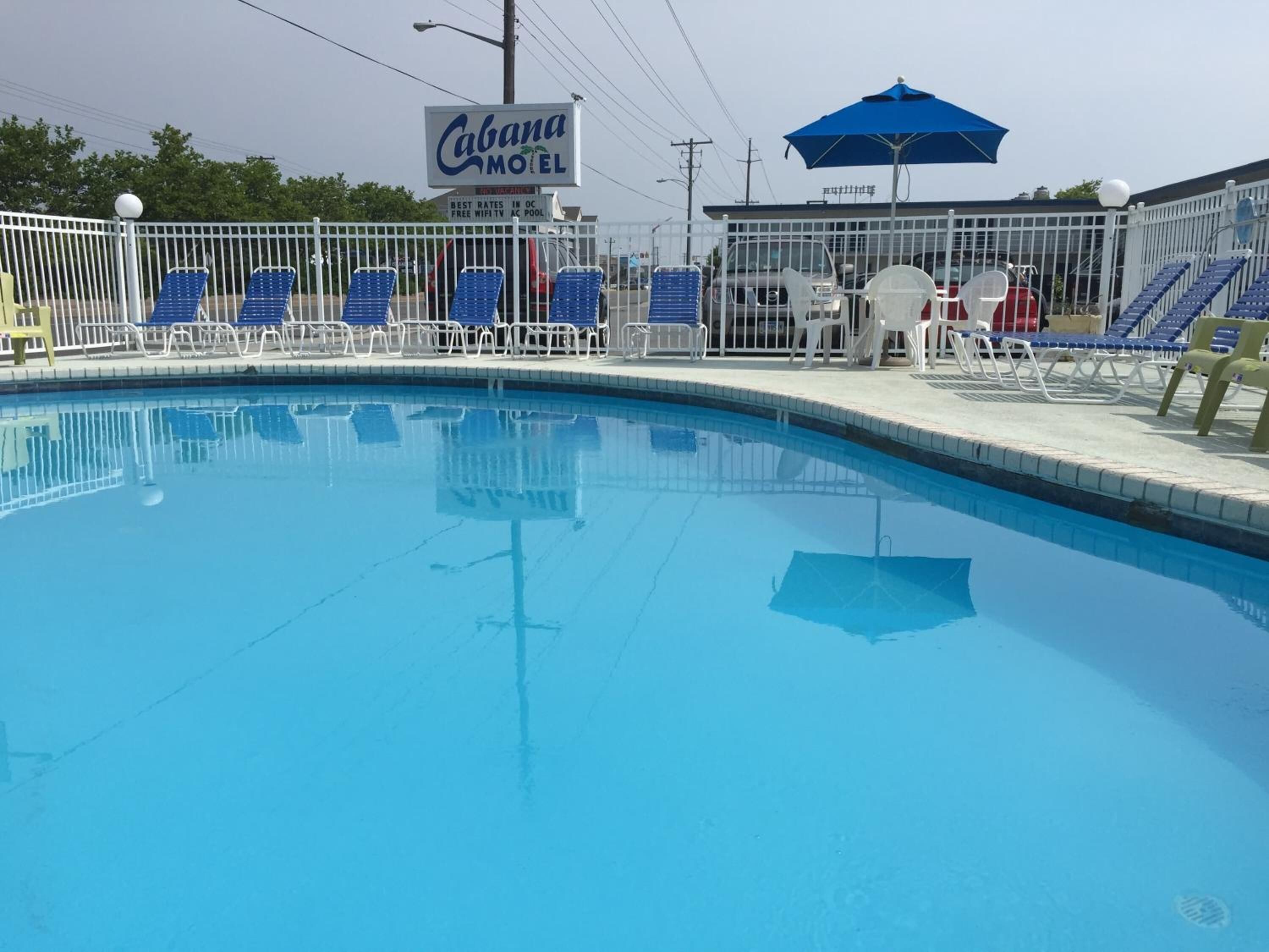 Ein Swimmingpool mit Liegestühlen und einem blauen Sonnenschirm, umgeben von einem weißen Zaun.