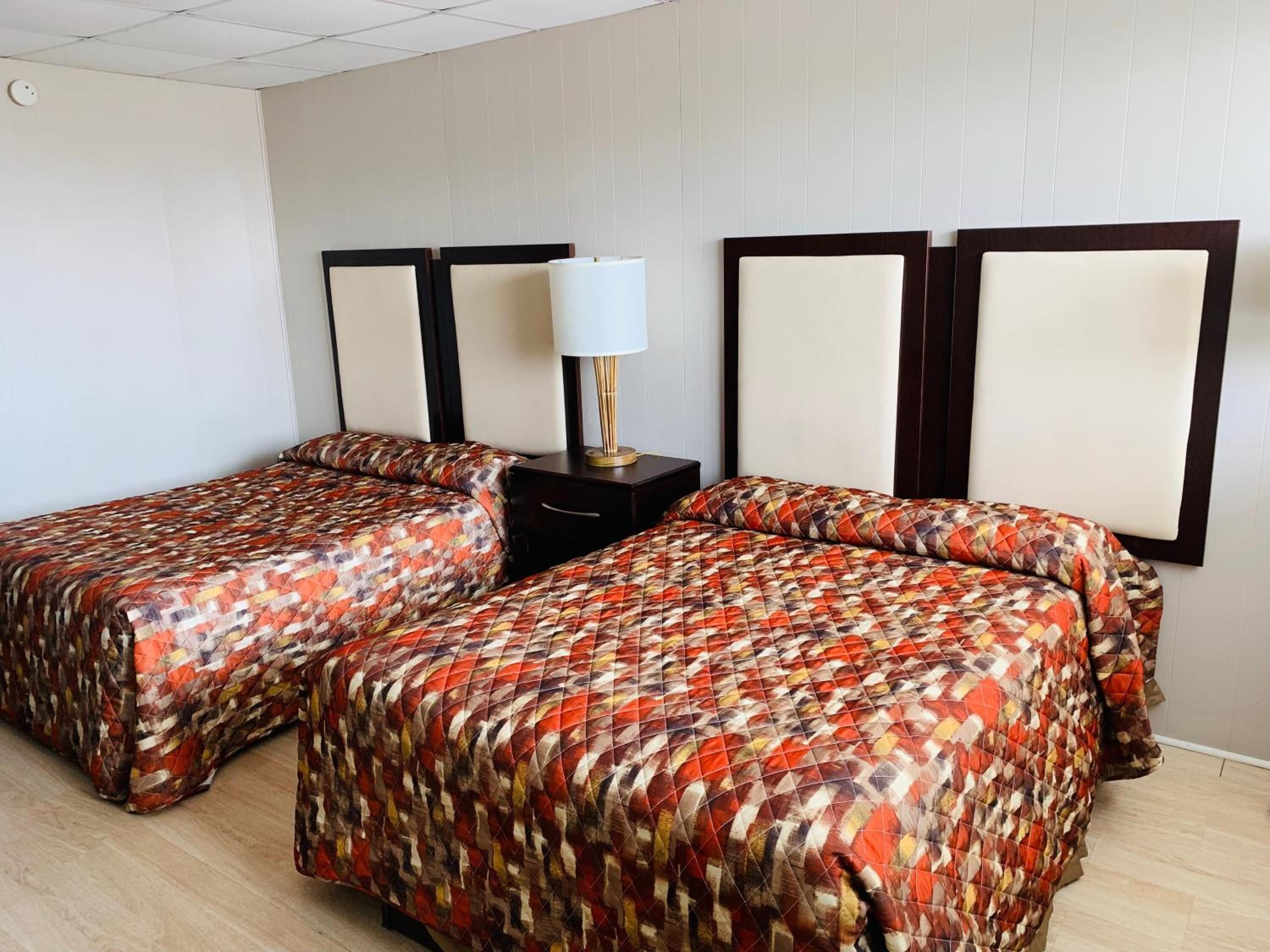 A hotel room with two beds, a nightstand, and a lamp.