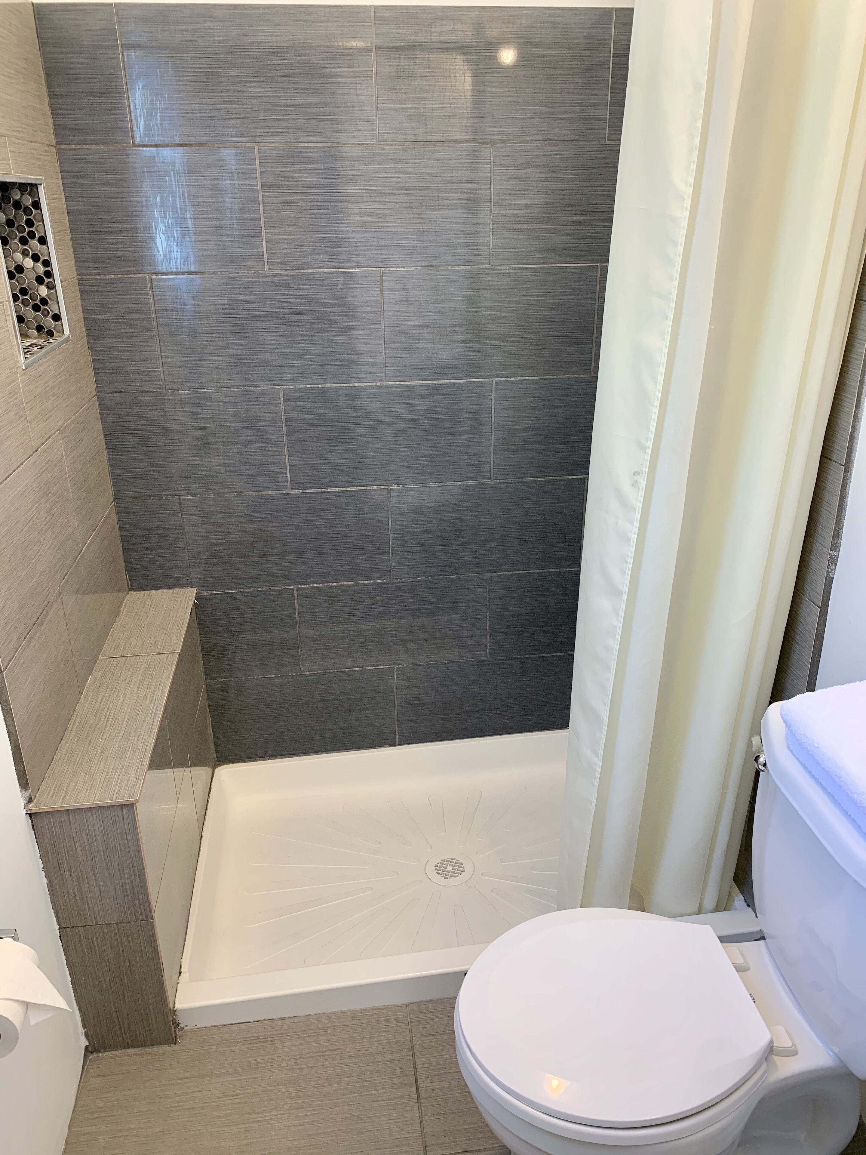 A bathroom with a shower, toilet, and a tiled wall.