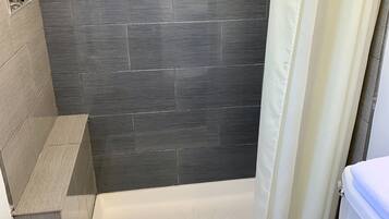 A bathroom with a shower, toilet, and a tiled wall.